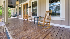 Une véranda couverte avec un plancher en bois, des fauteuils à bascule et une table.