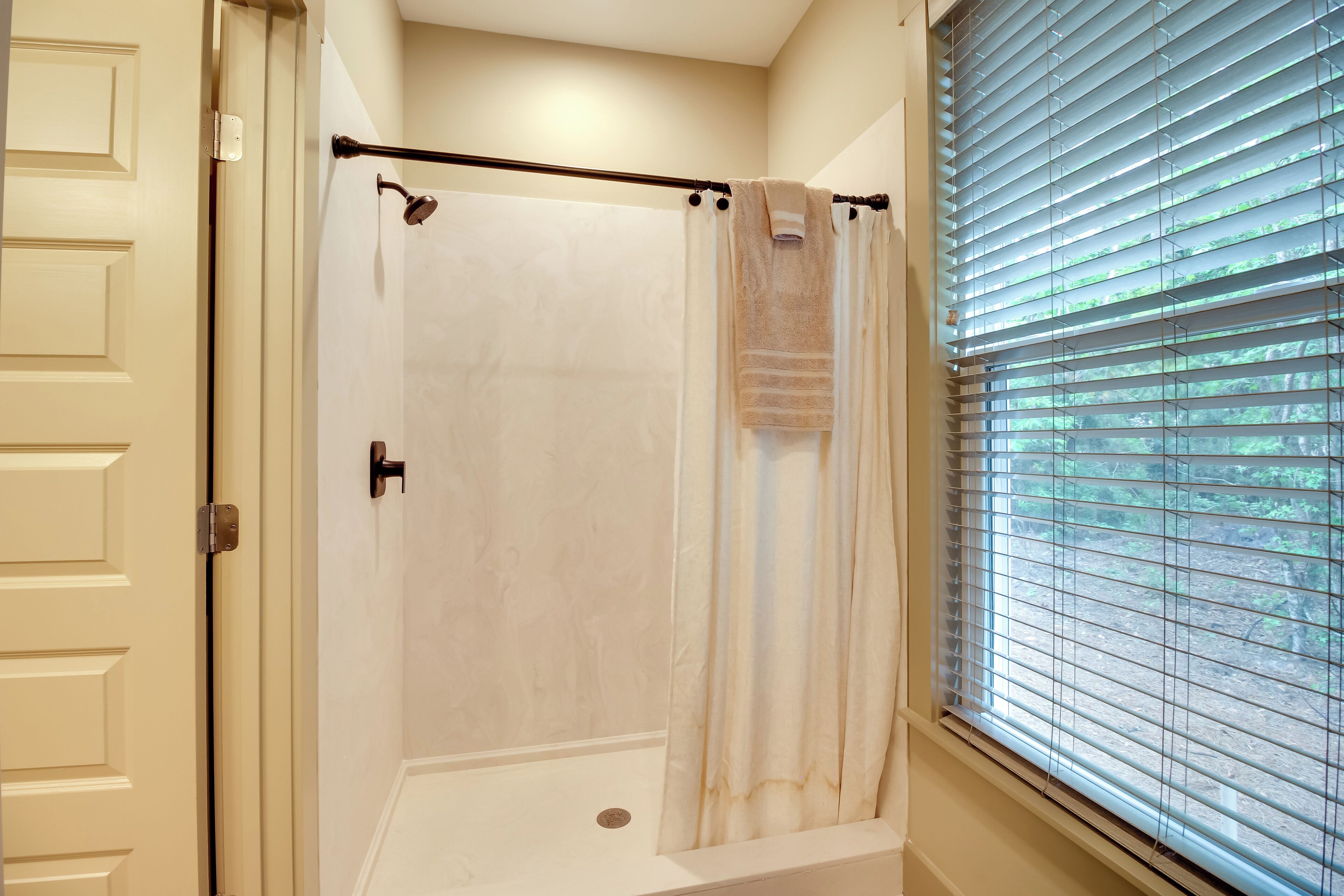A walk-in shower with a towel rack and a window with blinds.