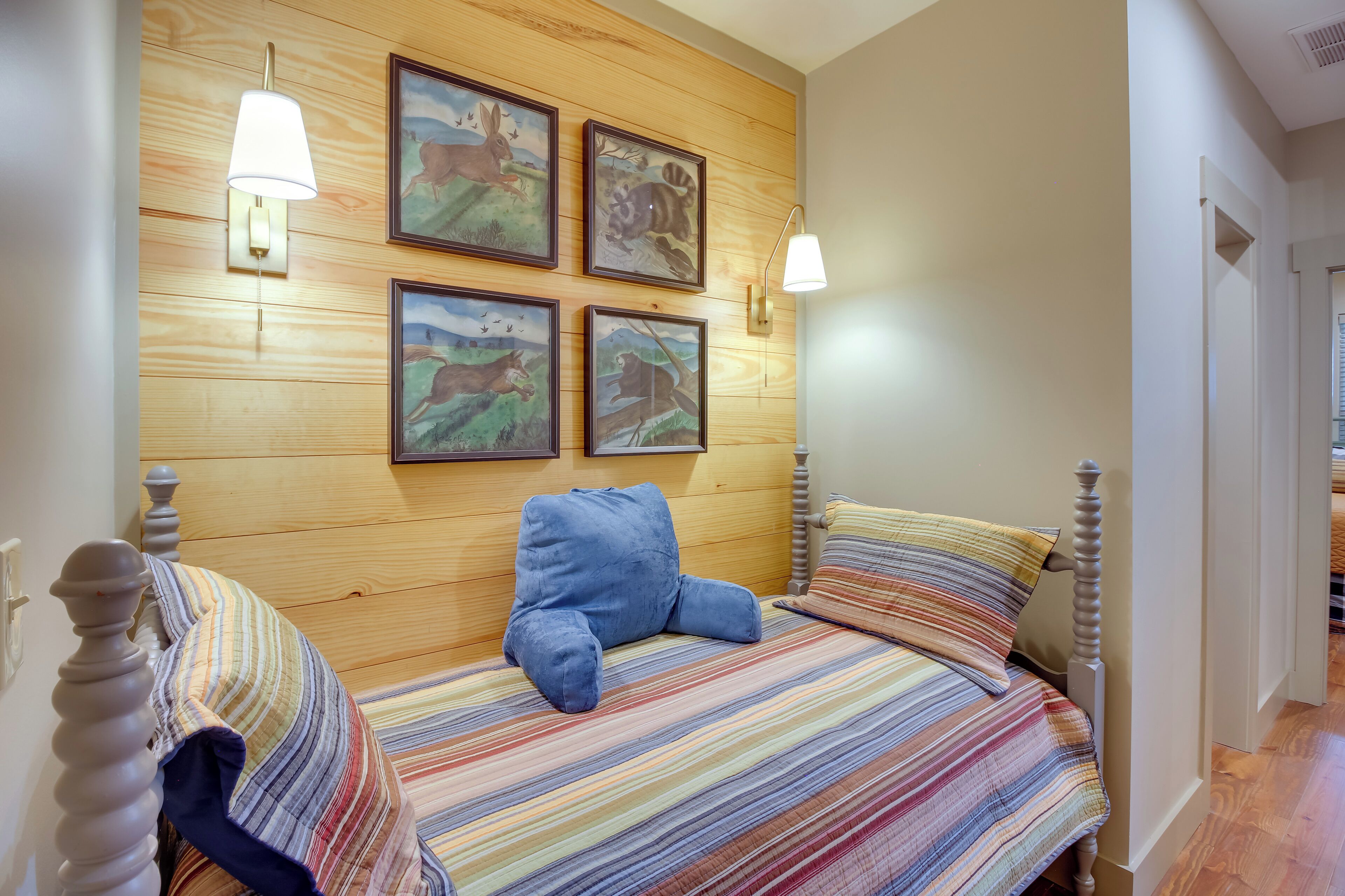 A bedroom with a wooden headboard, a striped bedspread, and four framed animal paintings on the wall.