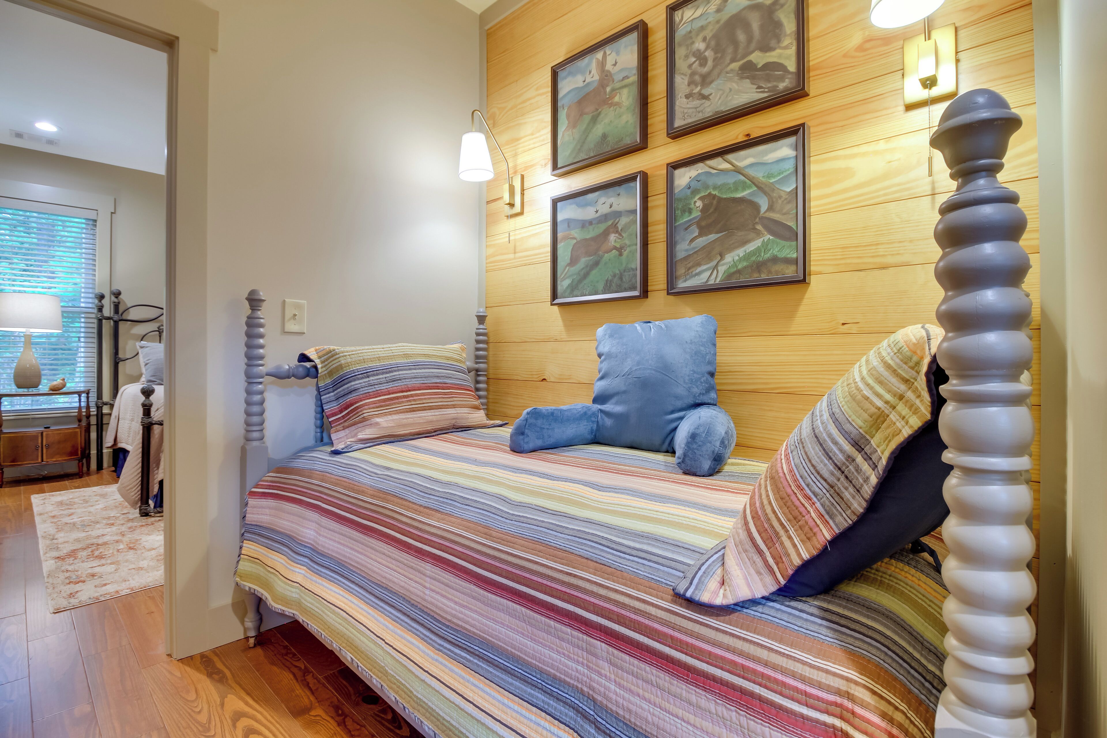 A bedroom with a wooden headboard, a striped bedspread, and four framed pictures on the wall.