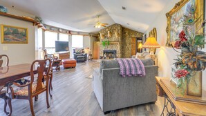 A spacious living room with a stone fireplace, a dining area with wooden furniture, and a cozy seating area with a grey sofa and a decorative lamp. - Buckhead Cabin w/ Fireplaces & Private Pool! (Buckhead)