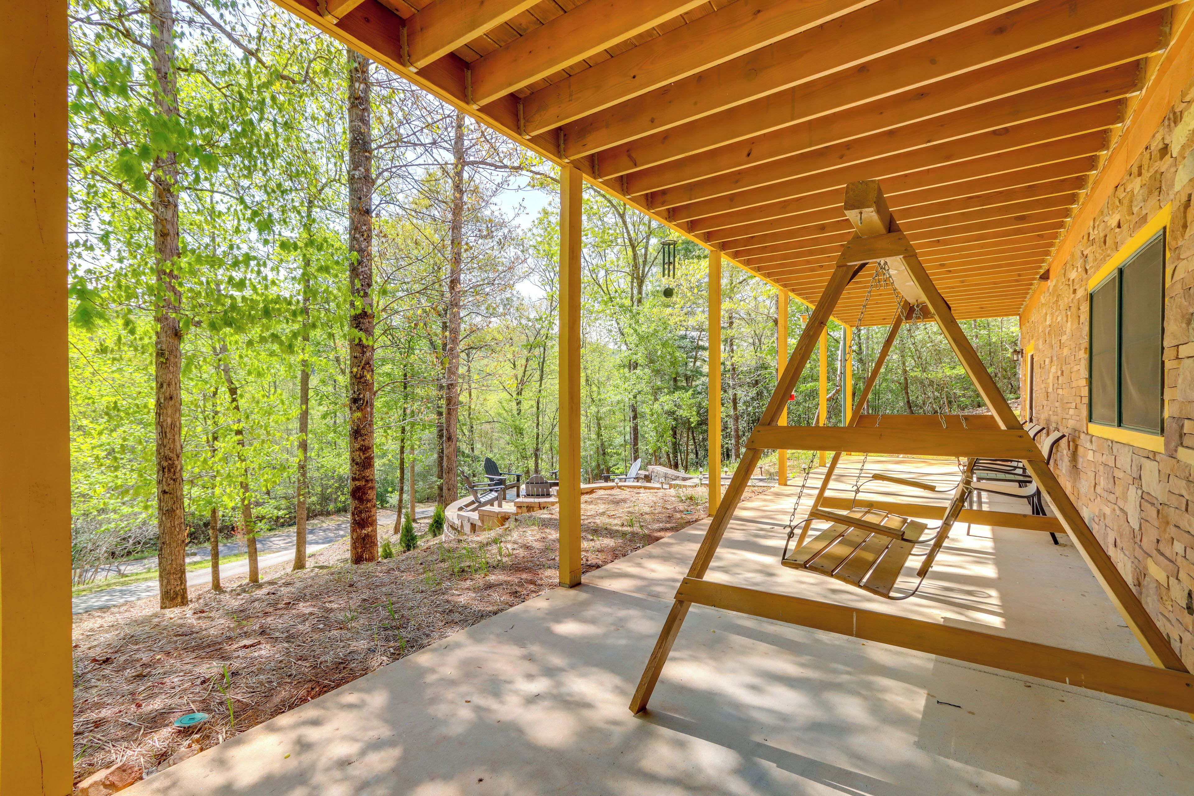 Un espacio al aire libre cubierto con un columpio de madera, rodeado de árboles y un edificio de piedra.