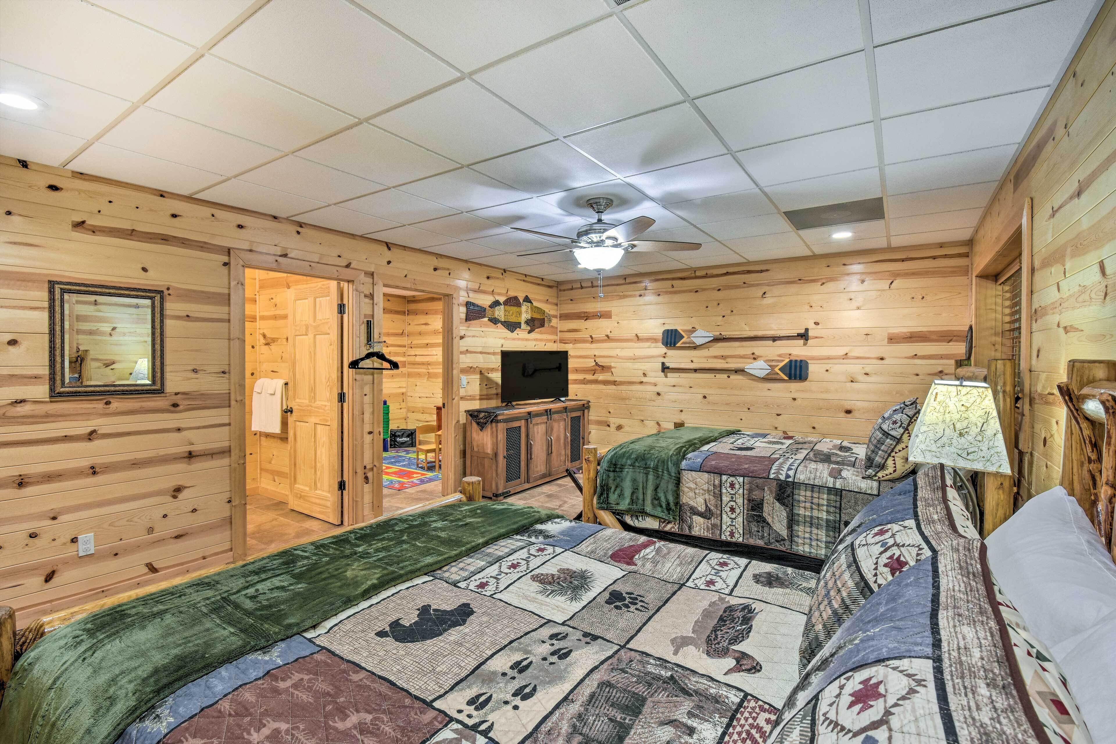 A cozy room with wooden walls, a ceiling fan, a television, and two beds with quilts.