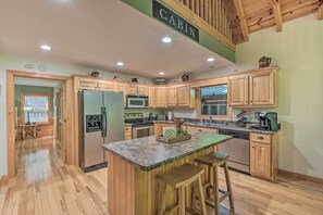 A spacious kitchen with wooden cabinets, a granite countertop, and a central island with bar stools. - Lavish Hiawassee Cabin - Great for Families! (Hiawassee)