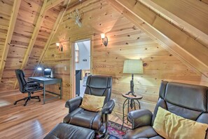 Une pièce mansardée chaleureuse avec des murs en bois, un bureau avec un ordinateur, deux fauteuils en cuir et une lampe.