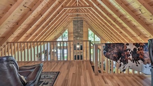 Amplia habitación en el ático con vigas de madera, chimenea de piedra y alfombra de cuero de vaca.