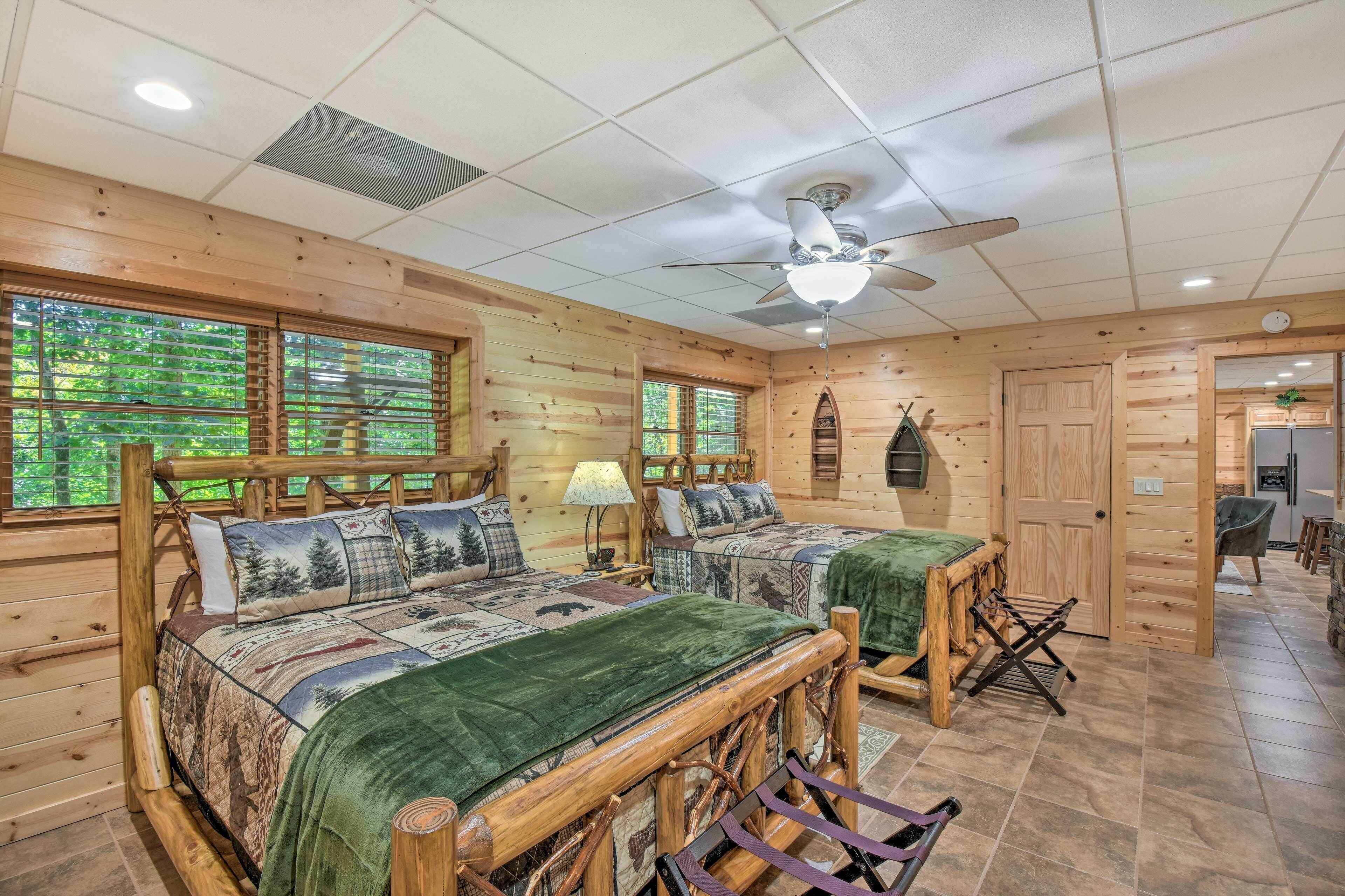 A log cabin-style bedroom with two beds, a ceiling fan, and a view of the outdoors through large windows.