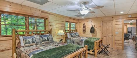 A log cabin-style bedroom with two beds, a ceiling fan, and a view of the outdoors through large windows.