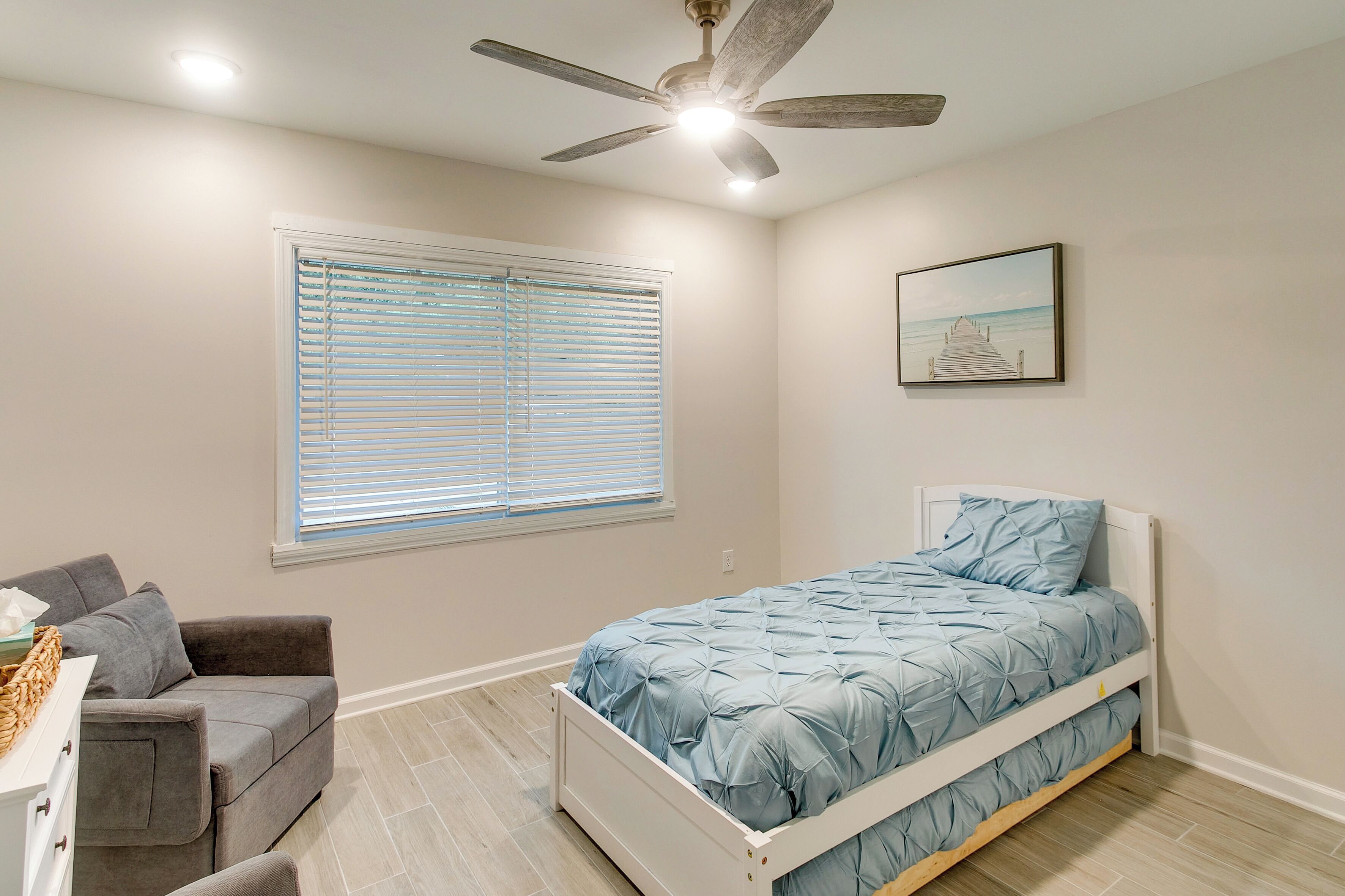 Un dormitorio con una cama, ventilador de techo, ventana con persianas, sofá y un cuadro en la pared.