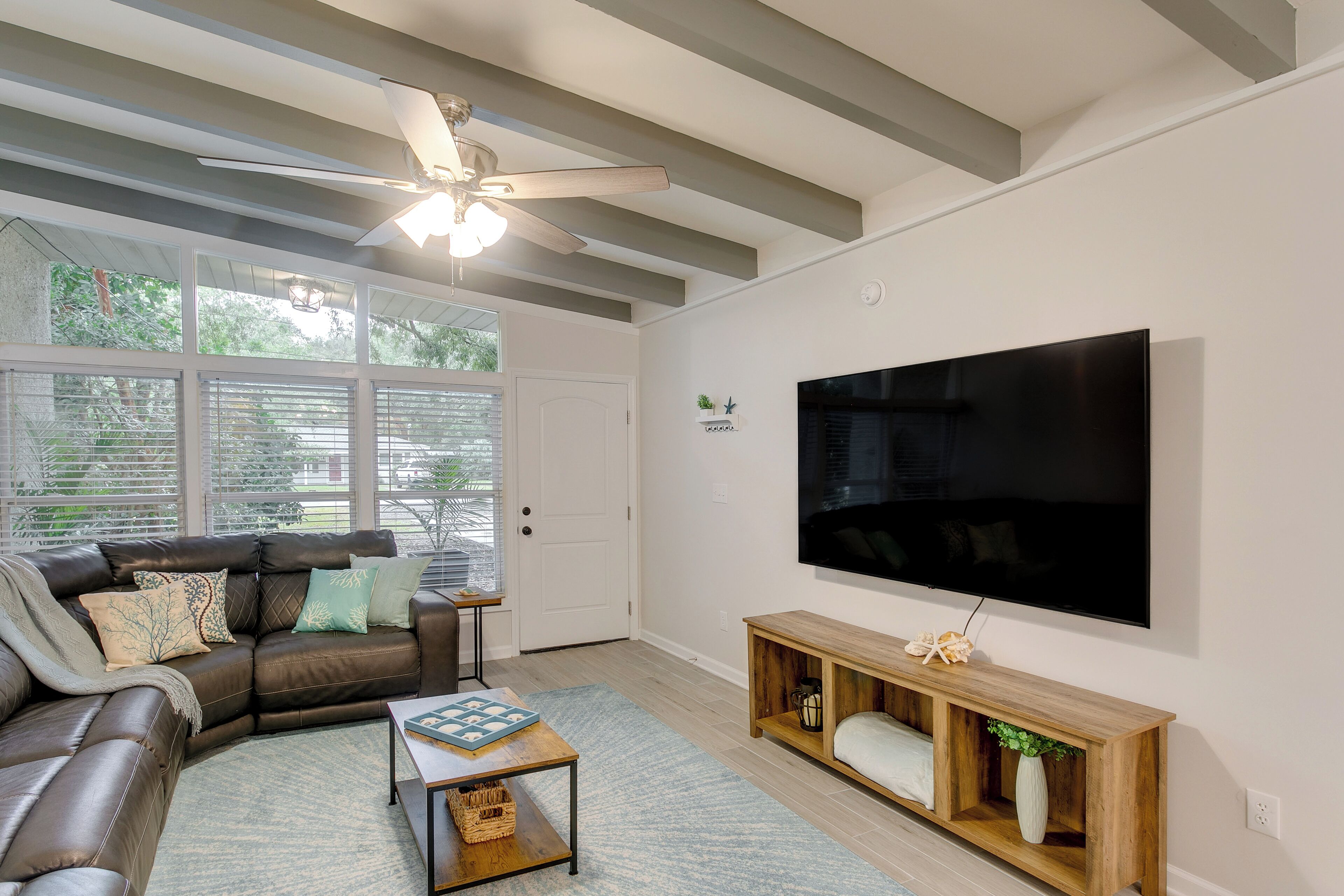 Een moderne woonkamer met een hoekbank, een salontafel, een houten console en een grote flatscreen televisie aan de muur.