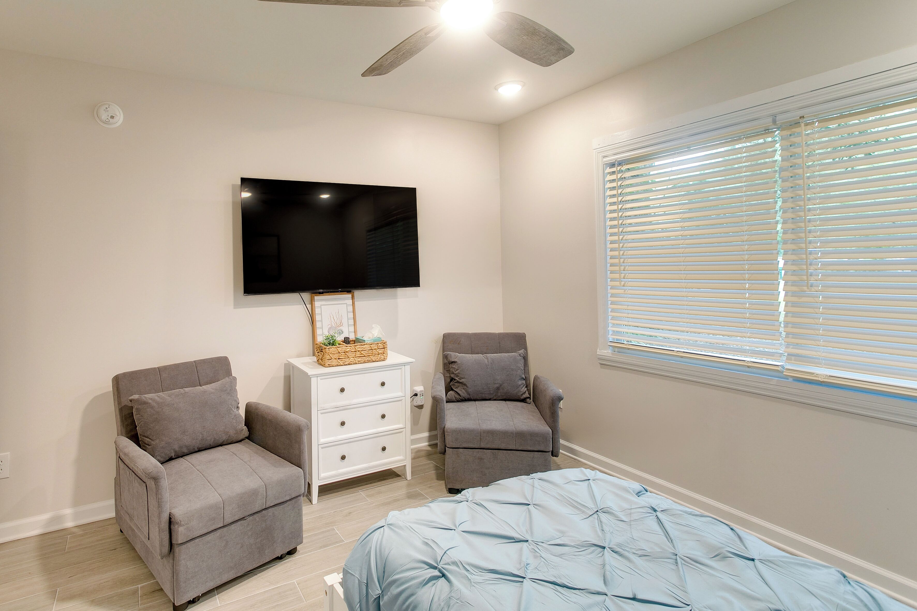 Une chambre à coucher avec un lit, deux fauteuils, un téléviseur et une fenêtre avec des stores.