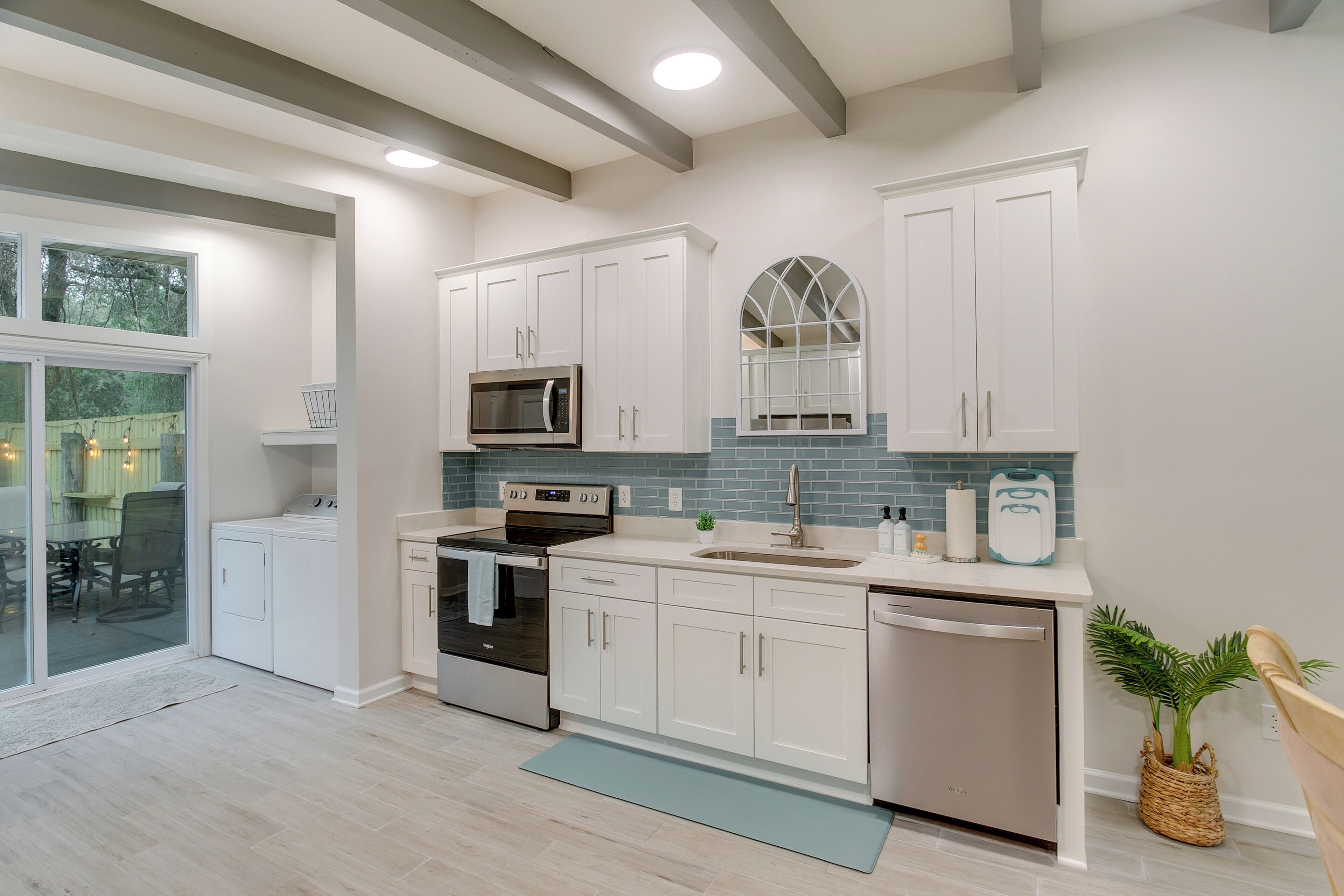 A modern kitchen with white cabinets, a stainless steel dishwasher, and a large window.