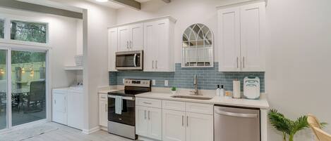 A modern kitchen with white cabinets, a stainless steel dishwasher, and a large window.