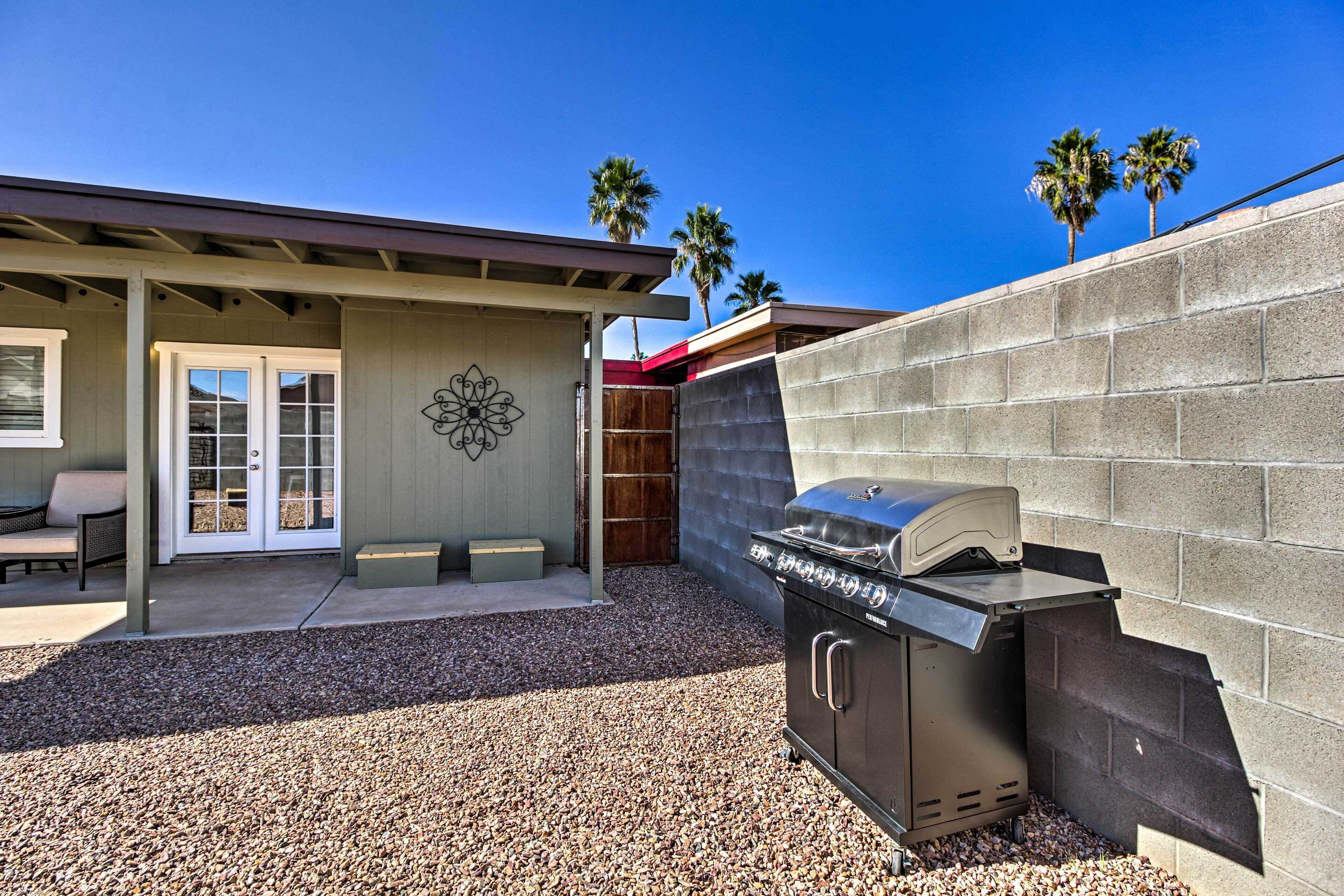 A backyard with a barbecue grill, a patio with seating, and a wall with palm trees.