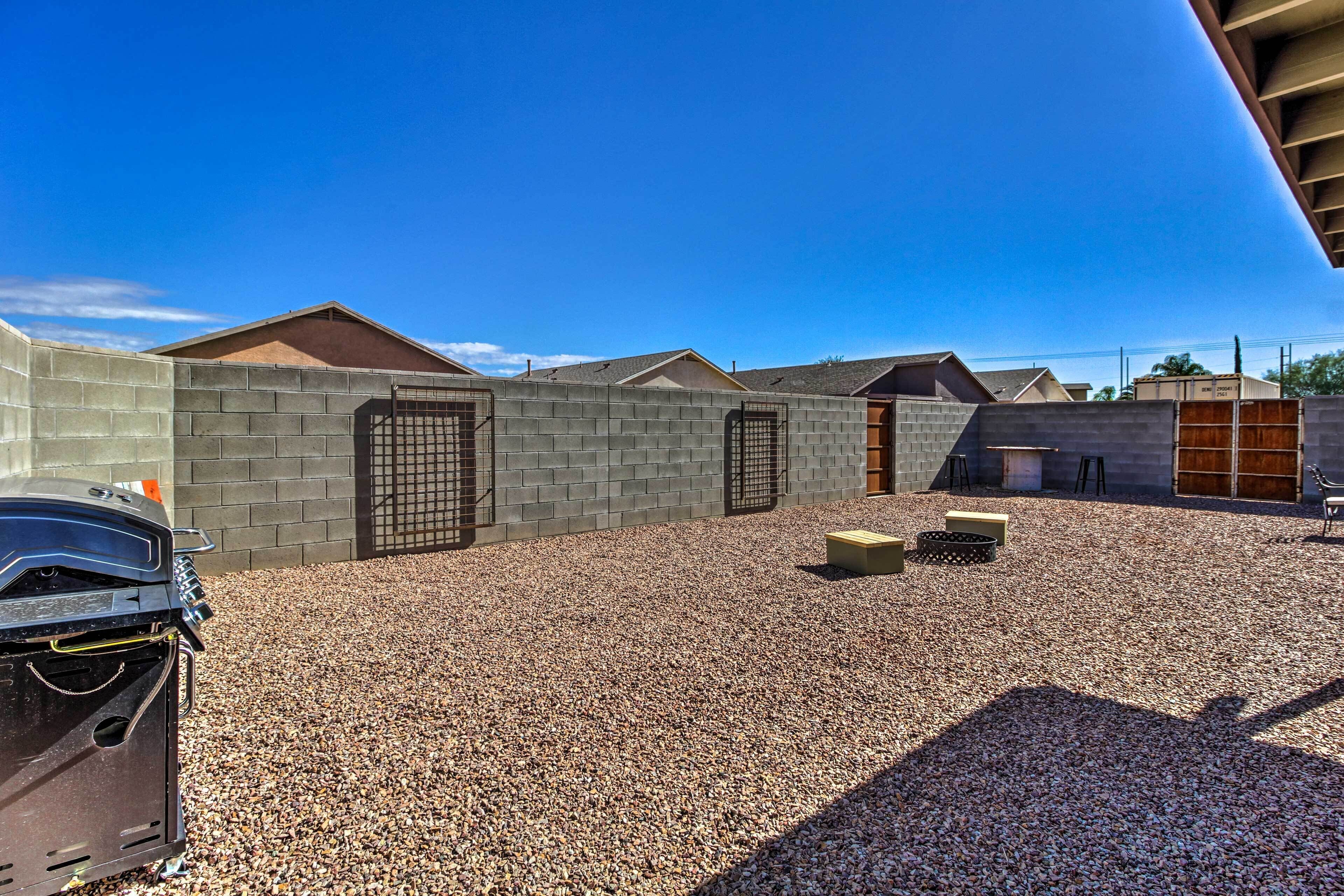 A gravel-covered outdoor area with a barbecue grill, a concrete wall, and a wooden bench.