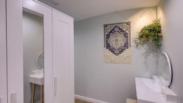 A bathroom with a white vanity, a hanging mirror, a wall-mounted plant, and a decorative tapestry.