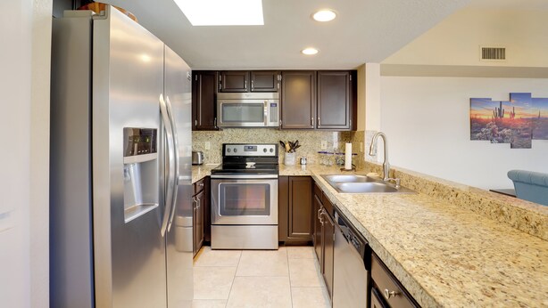 A modern kitchen with stainless steel appliances, granite countertops, and a cityscape painting on the wall. - Sunny Tucson Townhome w/ Patio & Mountain Views! (Tucson)