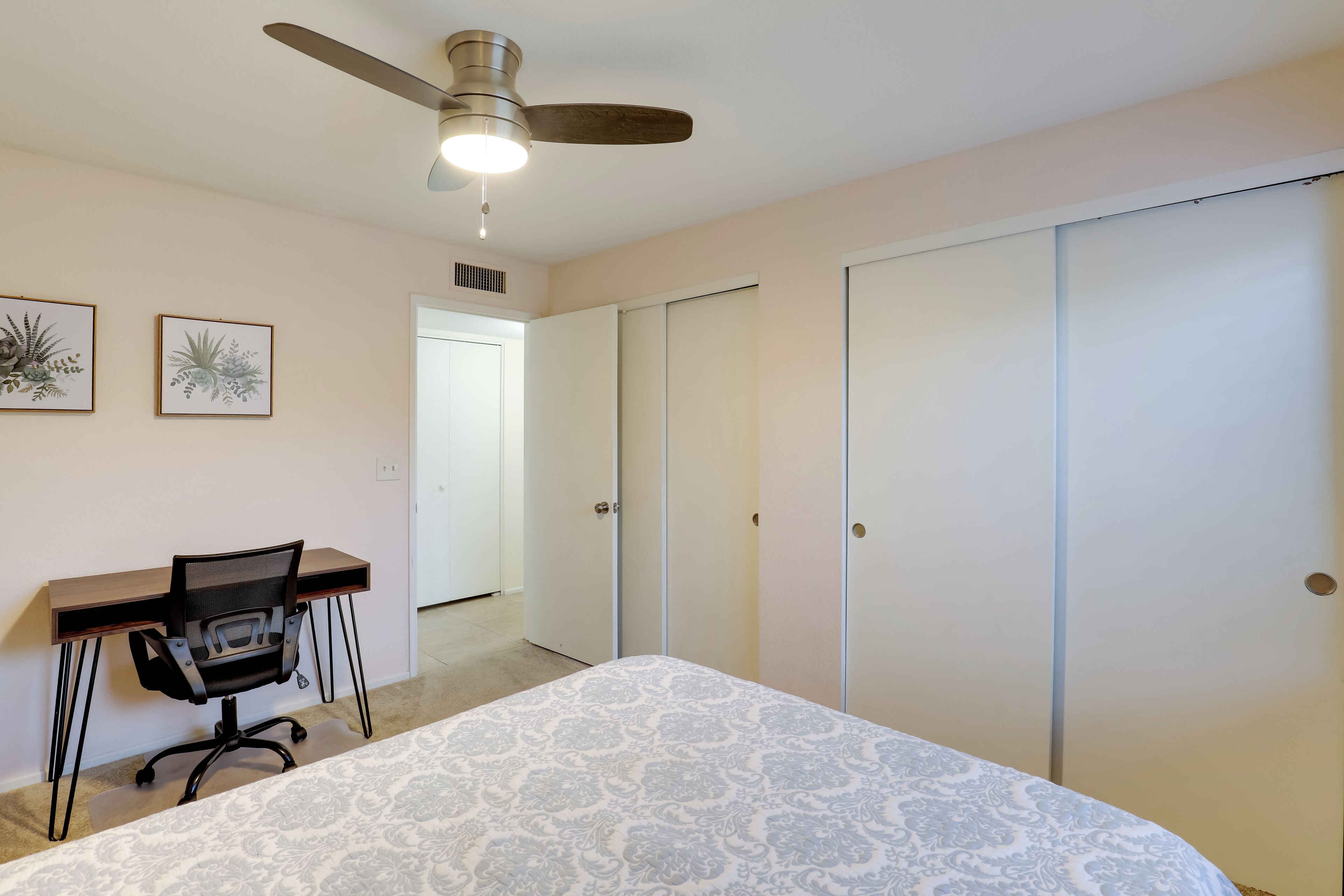A bedroom with a bed, a desk with a chair, a ceiling fan, and a wardrobe.