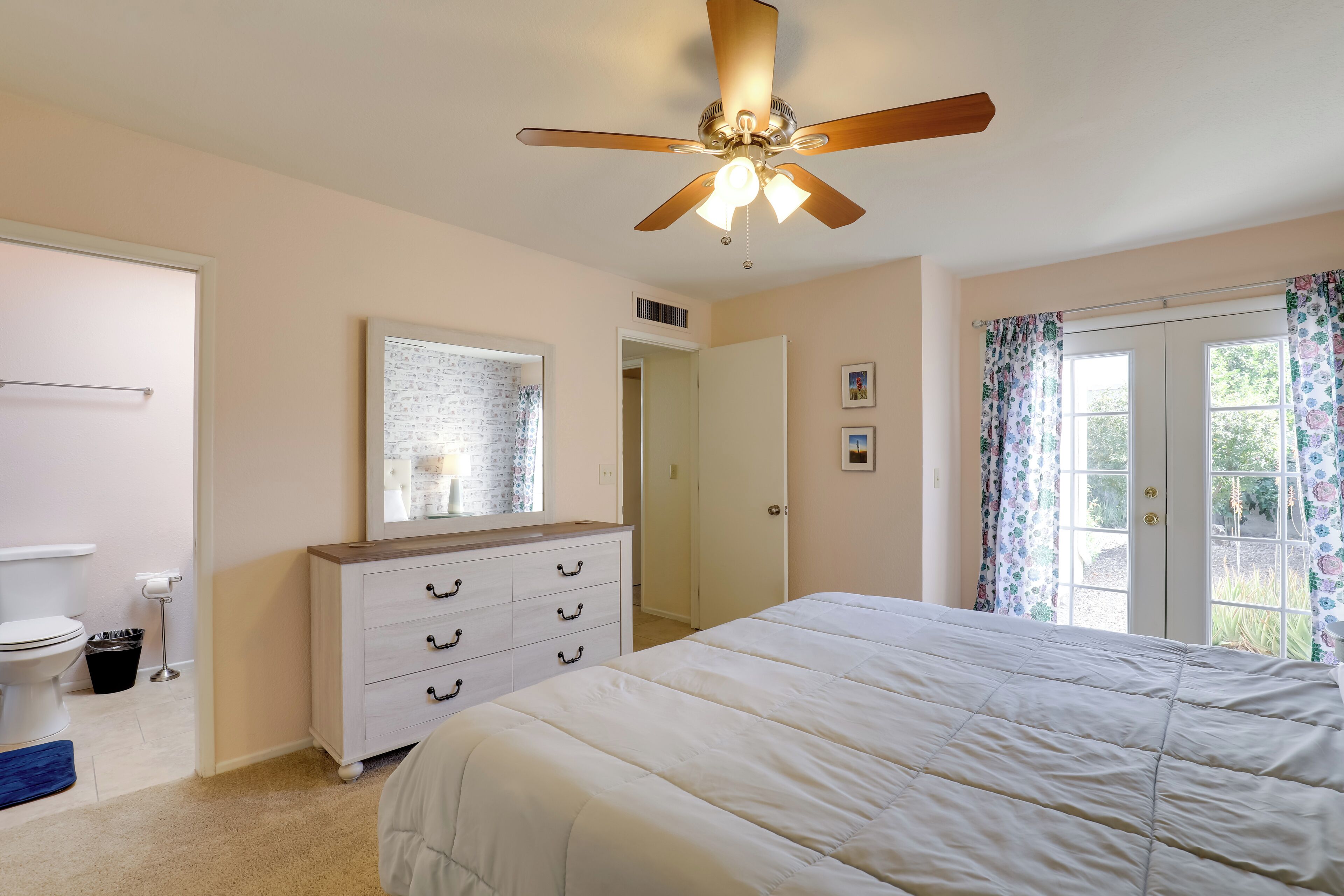 A bedroom with a bed, a dresser, a ceiling fan, and a window with curtains.