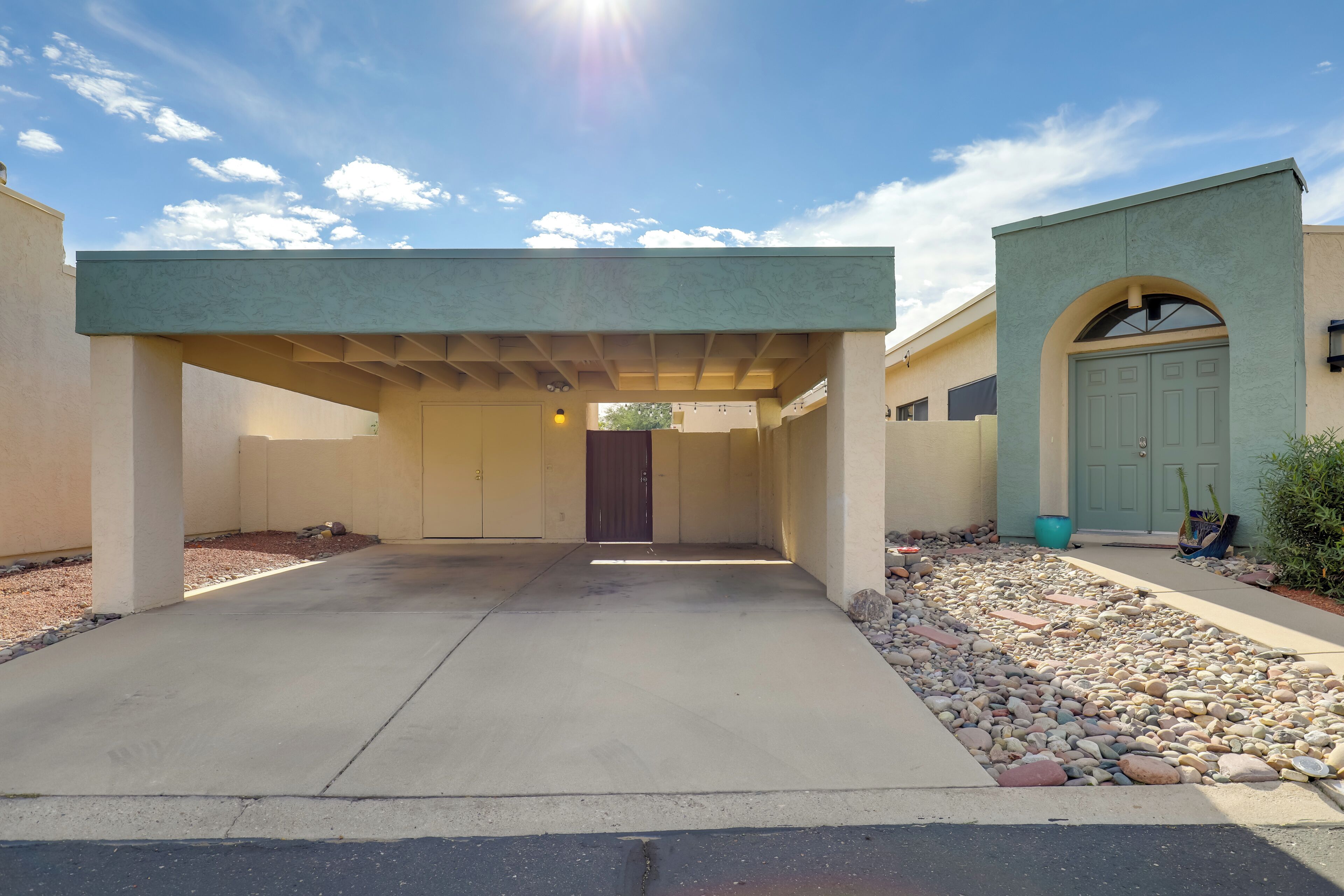 A covered driveway leading to a building with a green door and a covered entryway.