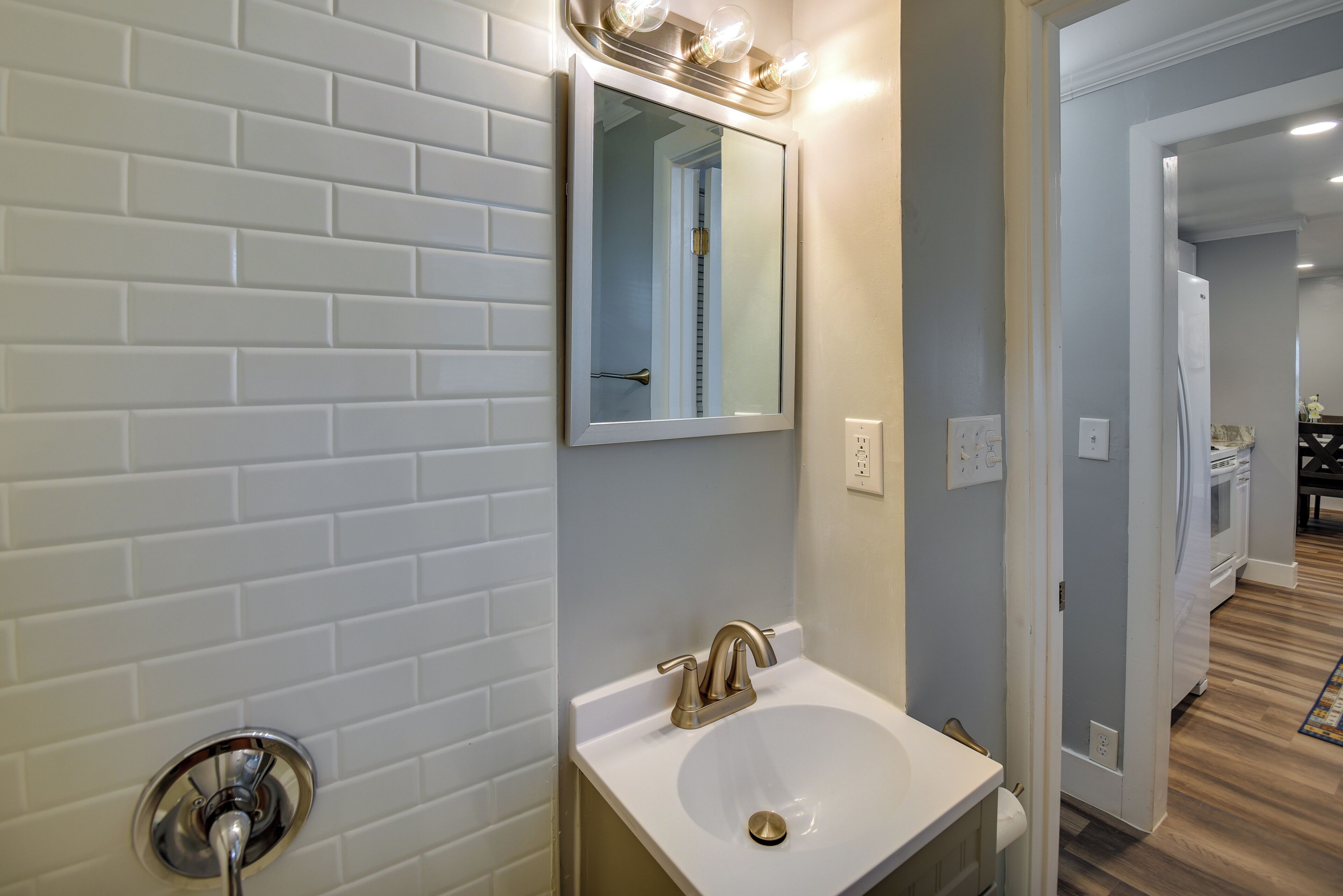 A bathroom with a white sink, a mirror with lights, and a white brick wall.