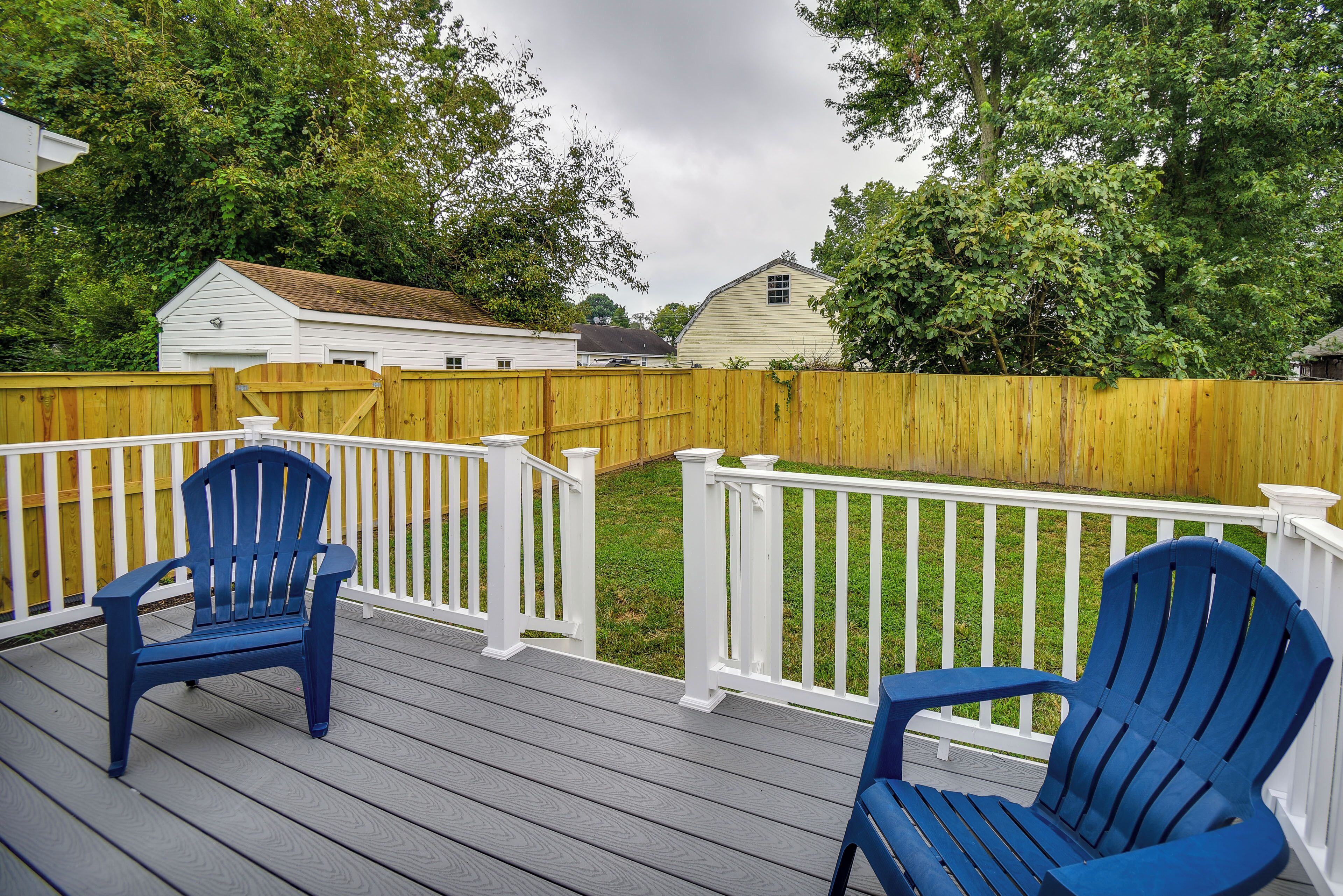 A wooden deck with two blue Adirondack chairs and a white railing.