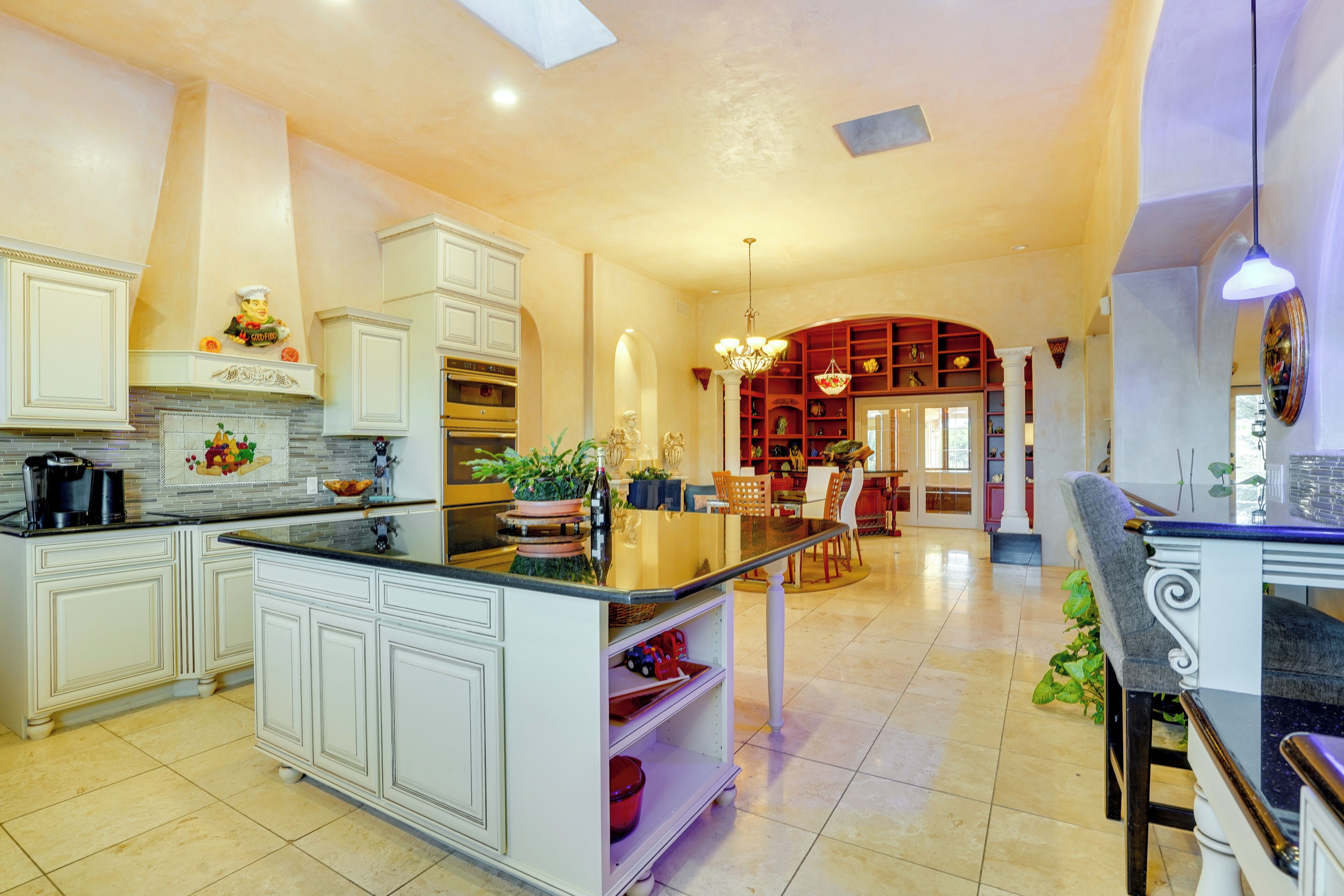 A spacious kitchen with white cabinetry, a central island, and a dining area with a chandelier.