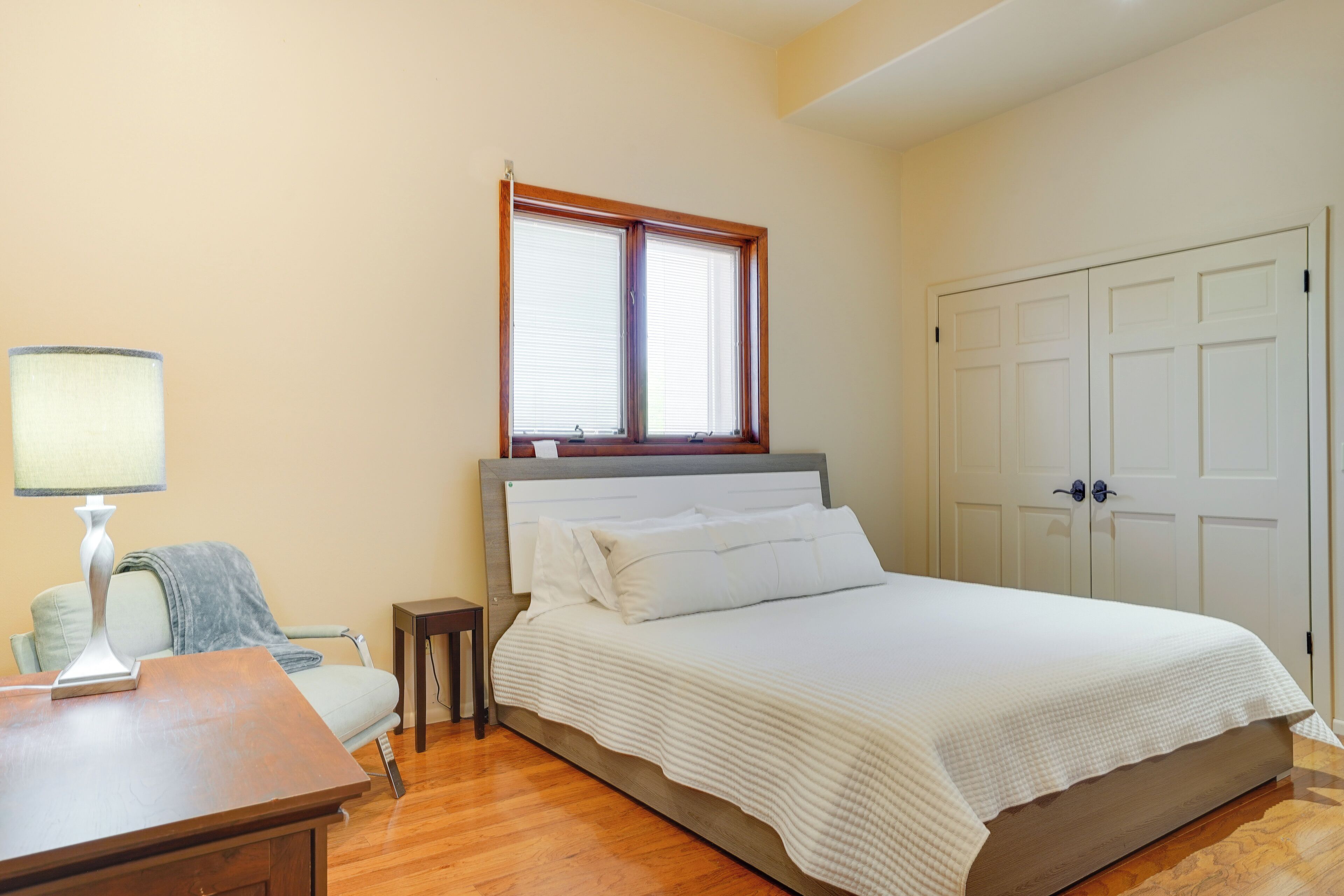 Une chambre à coucher avec un lit, une table de chevet, une lampe, une chaise et une fenêtre.