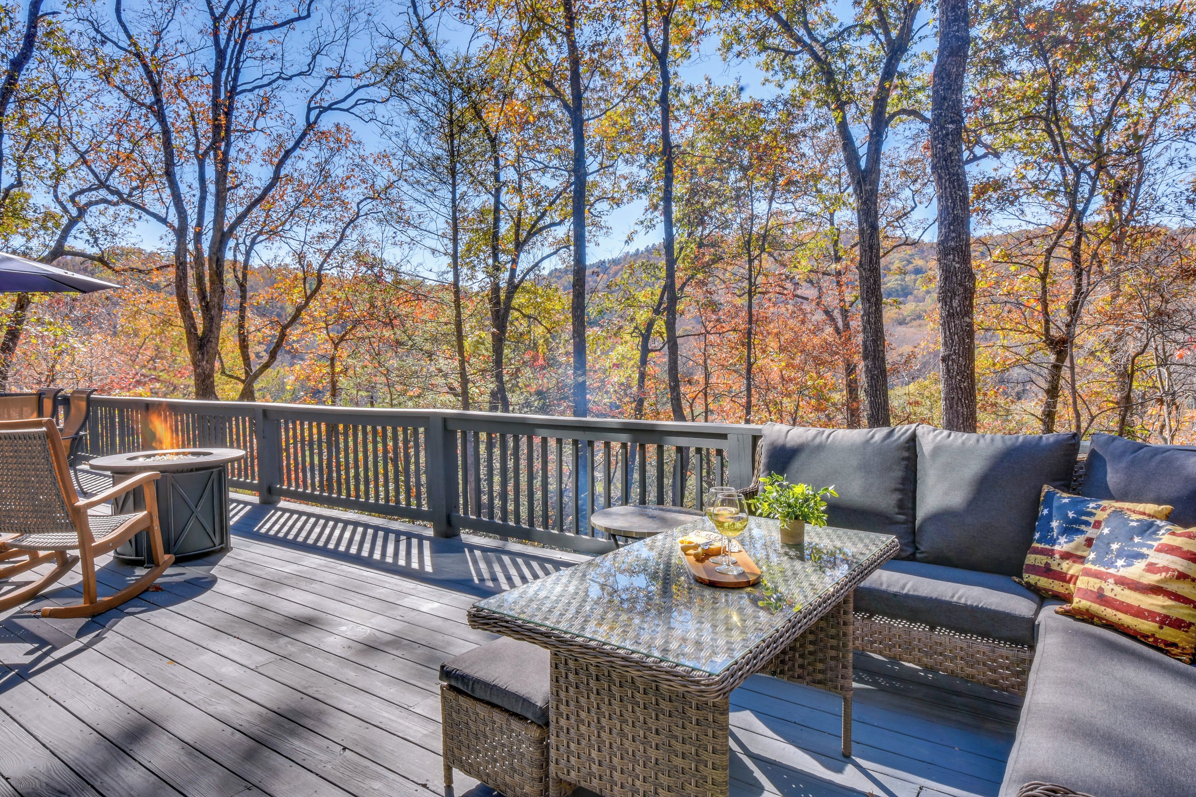 A wooden deck with a wicker sofa, a round table, and a fire pit.
