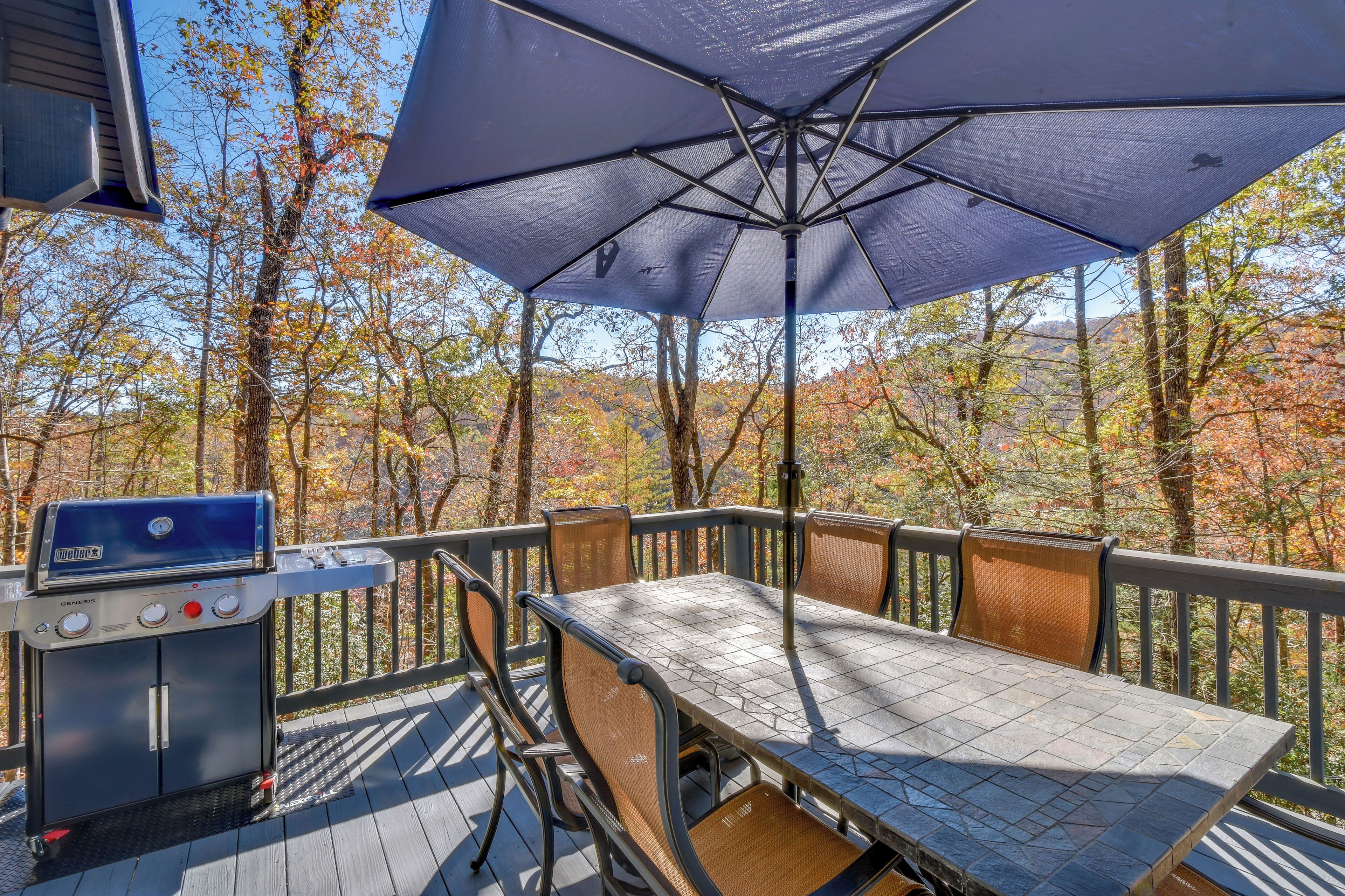 A deck with a grill, table, chairs, and a large umbrella.