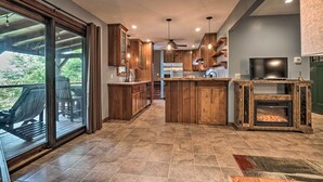 Een moderne keuken met houten kasten, een centraal eiland, een ingebouwde open haard en een grote schuifpui die uitkomt op een terras.