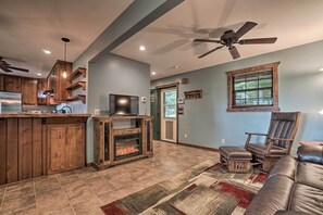 A spacious living area with a fireplace, a large leather sofa, and a wooden entertainment center. - Yellow Mountain Blairsville Cabin w/ Scenic Deck (Blairsville)
