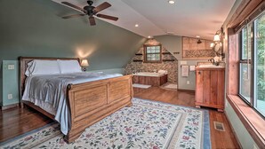 Een slaapkamer met een houten bed, een plafondventilator en uitzicht op een badkamer met een stenen muur en een houten wastafel.