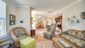 A living room with wicker furniture, a green ottoman, and a dining area with a table and chairs. - Hampton Condo: By Convention Center & Coliseum! (Hampton)