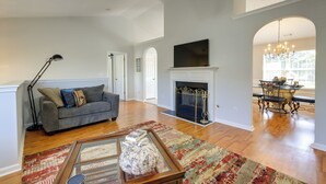 A spacious living room with a fireplace, a dining area with a chandelier, and a large window providing natural light. - Spacious Georgia Home w/ Deck, Grills & Fireplace! (Riverdale)