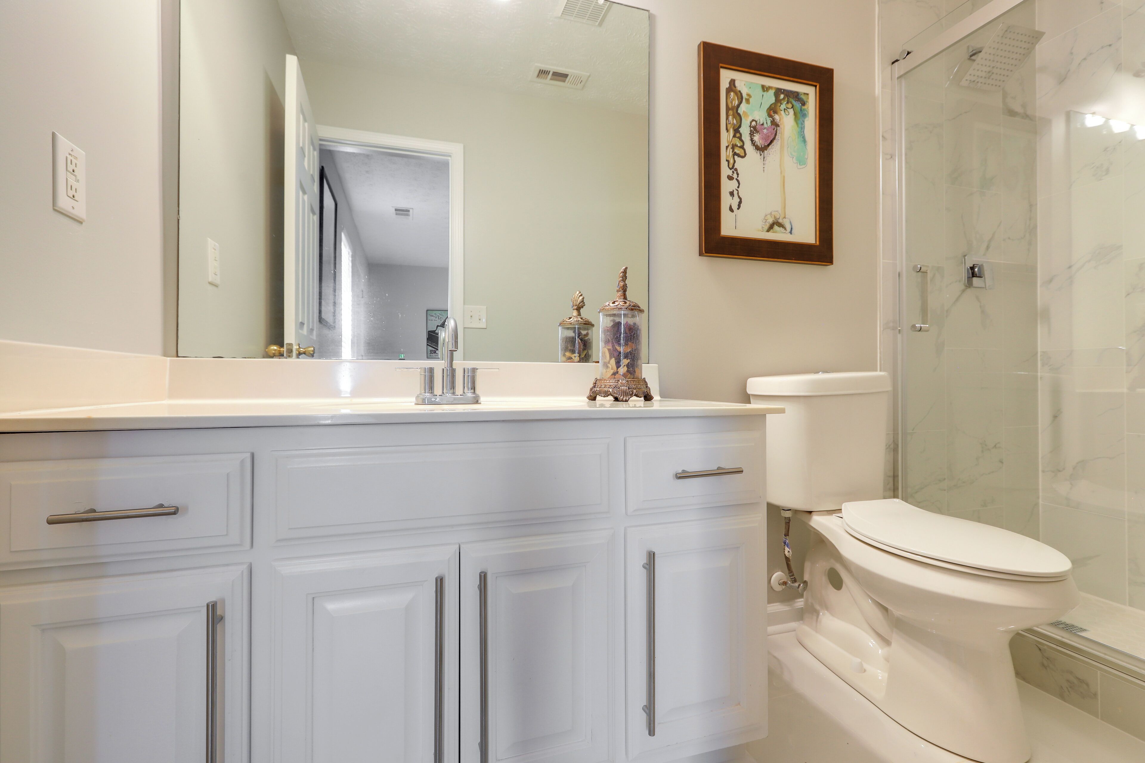 A bathroom with a white vanity, a toilet, a shower, and a mirror.