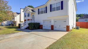 A two-story house with a front garage, a covered front porch, and a small front yard. - Spacious Georgia Home w/ Deck, Grills & Fireplace! (Riverdale)