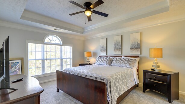 A bedroom with a bed, two bedside tables, a ceiling fan, a window, and artwork on the walls. - Spacious Georgia Home w/ Deck, Grills & Fireplace! (Riverdale)