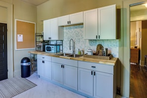 A compact kitchen with white cabinets, a wooden countertop, a stainless steel sink, and a microwave.