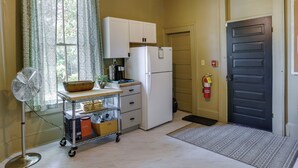A compact kitchen with a refrigerator, a small countertop, a fan, and a window with curtains. - Charming Thomasville Getaway: Walk to Downtown! (Thomasville)