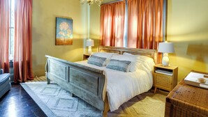 A bedroom with a wooden bed, two bedside tables, a chandelier, and a painting on the wall. - Charming Thomasville Getaway: Walk to Downtown! (Thomasville)