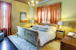 A bedroom with a wooden bed, two bedside tables with lamps, a painting on the wall, and a window with curtains.