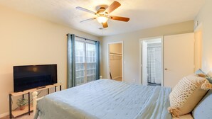 Ein Schlafzimmer mit einem Bett, einem Deckenventilator, einem Fernseher auf einem Schrank und einem Fenster mit Vorhängen.