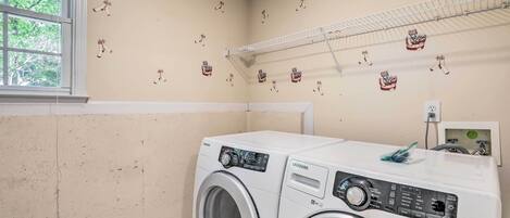 Un cuarto de lavandería con dos lavadoras Samsung VRT de carga frontal, un tendedero y una ventana con vista a árboles.