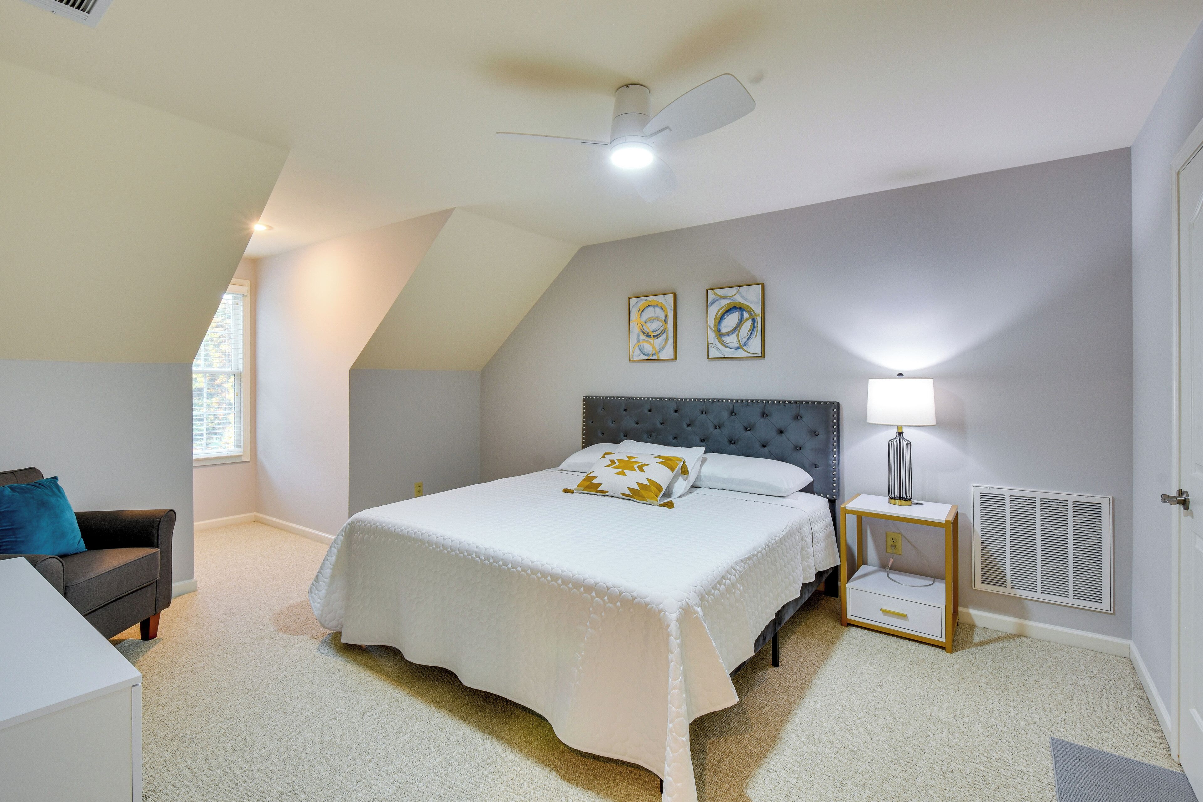 Ein Schlafzimmer mit einem Bett, einem Nachttisch, einer Lampe, einem Fenster und einem Deckenventilator.