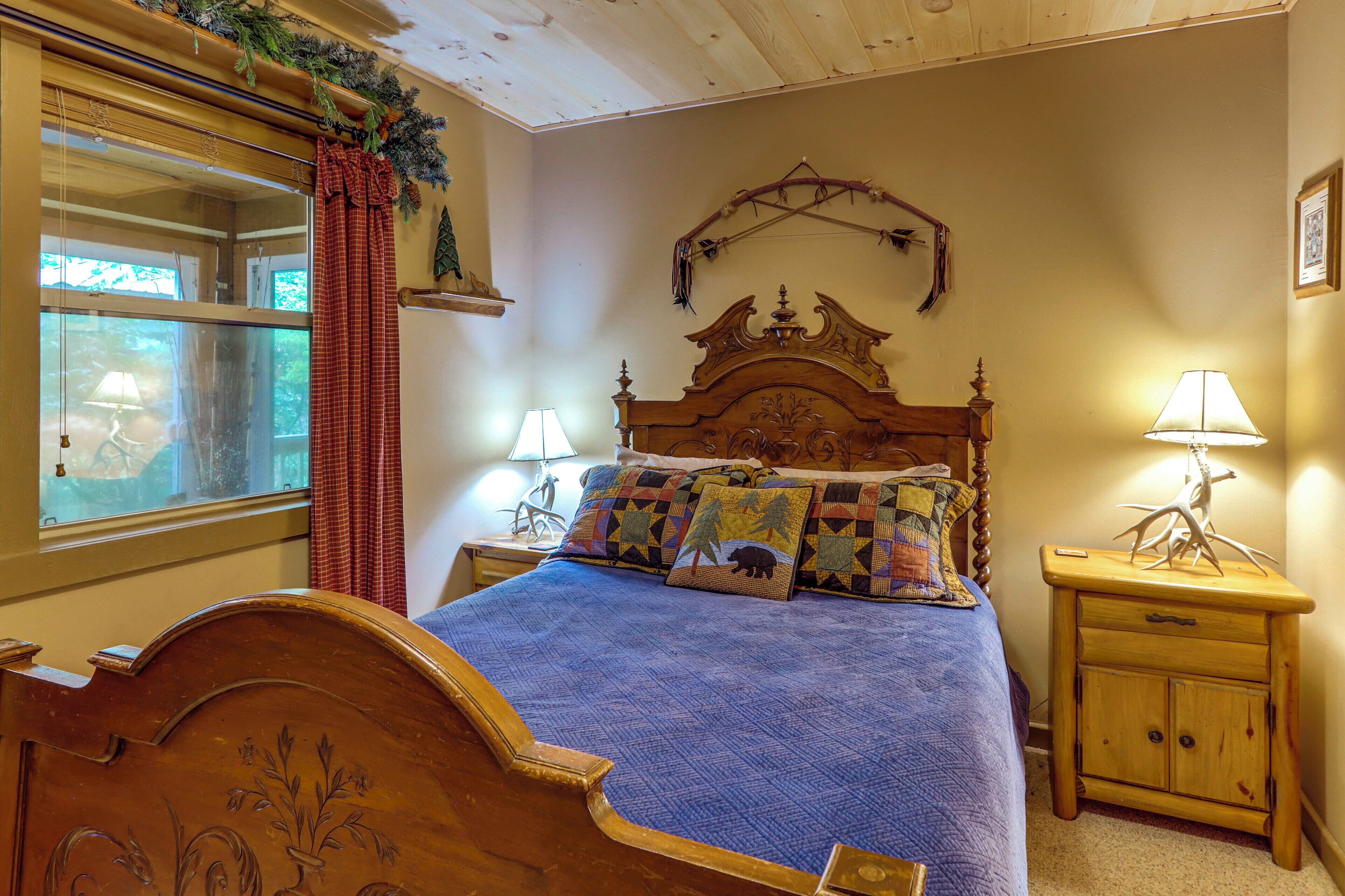 A bedroom with a wooden bed, a nightstand with a lamp, a window with curtains, and a wall-mounted decoration.