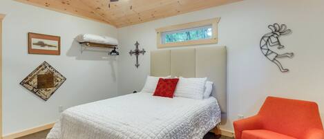 A bedroom with a bed, a red chair, a ceiling fan, a window, and wall decorations.