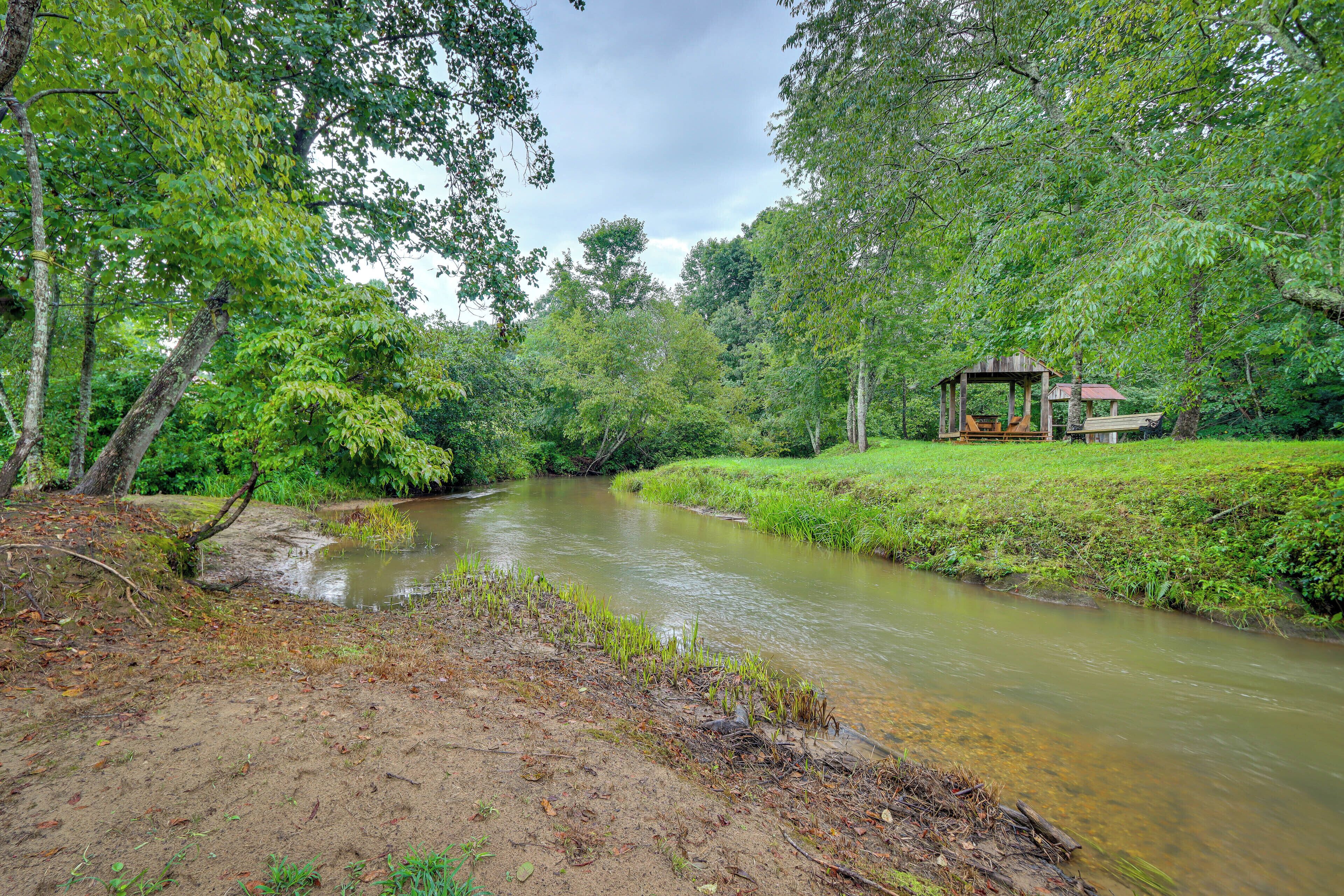 A river with a wooden structure on the right bank, surrounded by dense greenery.
