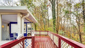 Eine Holzterrasse mit roter Geländer, weißen Gitterelementen und einem überdachten Sitzbereich mit blauen Wänden und weißen Stühlen.