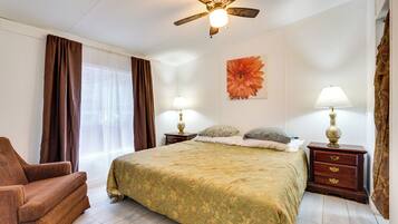 A bedroom with a bed, two nightstands, a ceiling fan, a chair, and a window with curtains.